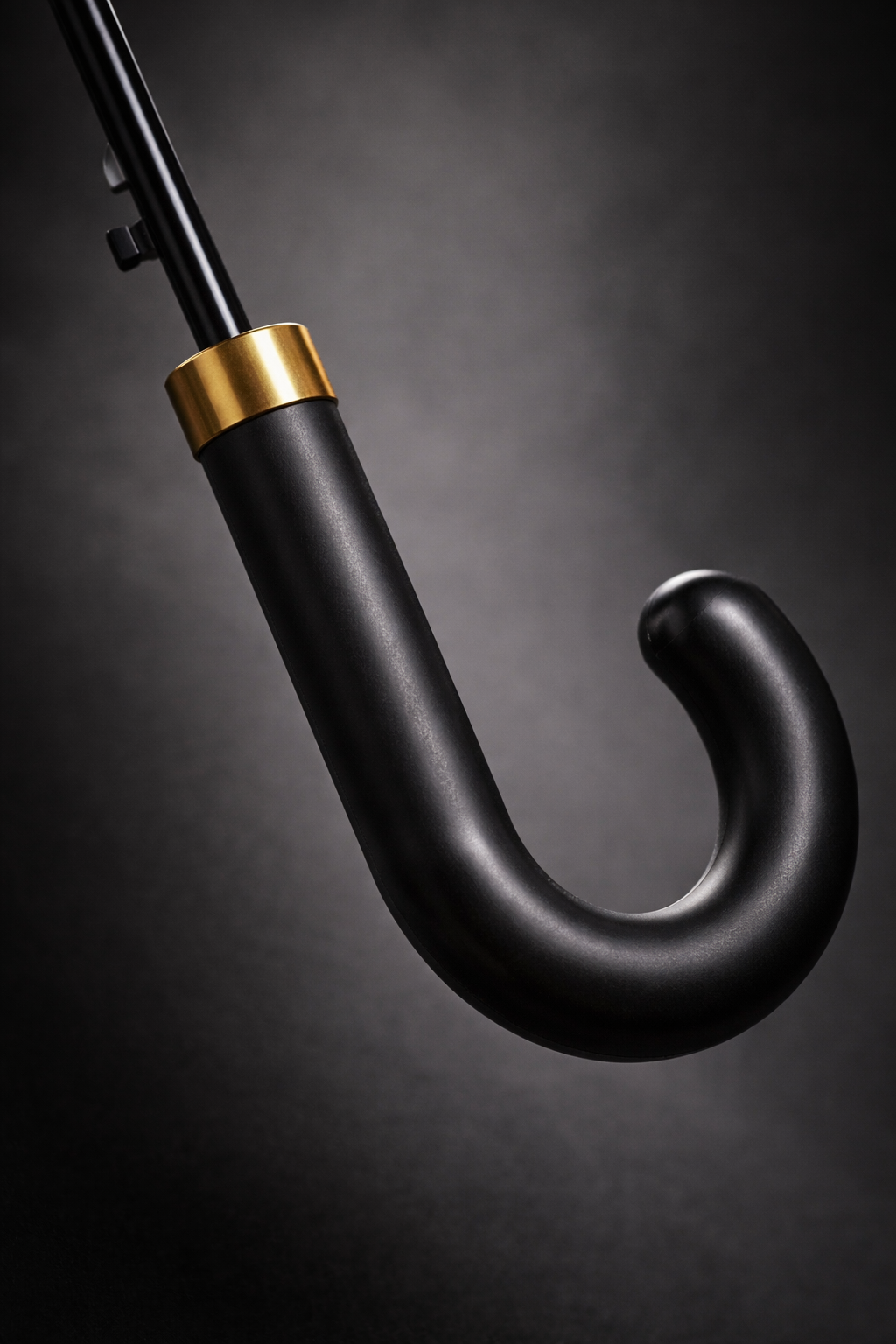 Close-up of black curved umbrella handle with brushed gold collar and matte shaft detail.