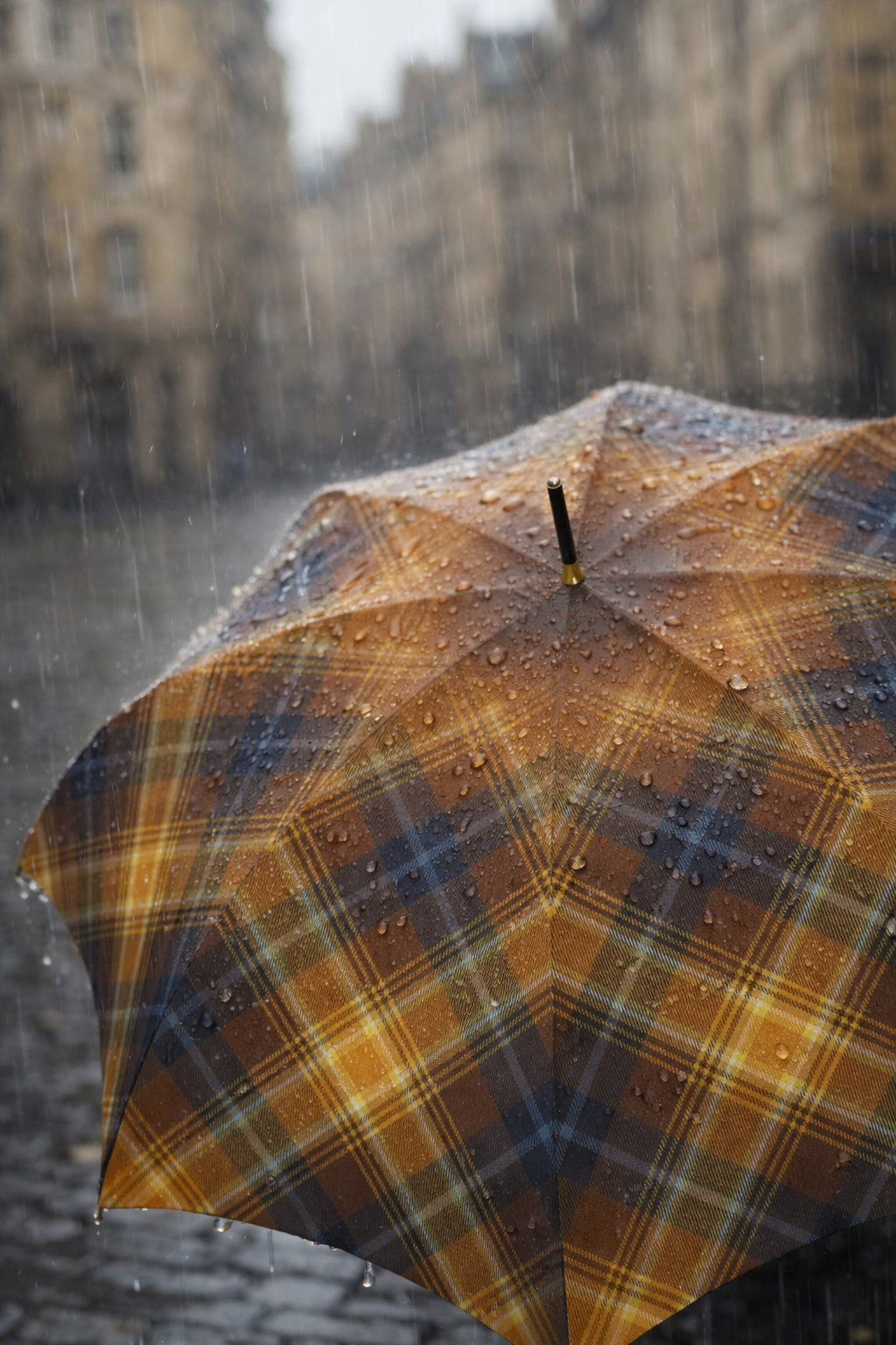 Close-up of tartan umbrella covered in rain droplets on a blurred urban street.