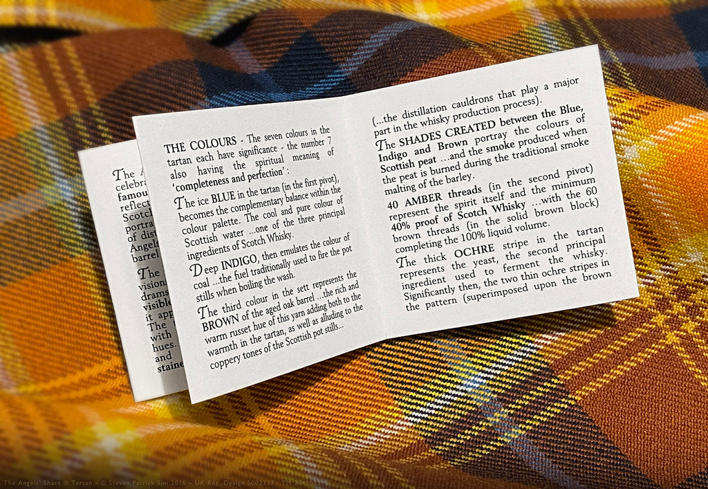 Open Angels’ Share tartan booklet page explaining the seven colours of the tartan and their symbolic meanings, photographed on the tartan cloth.