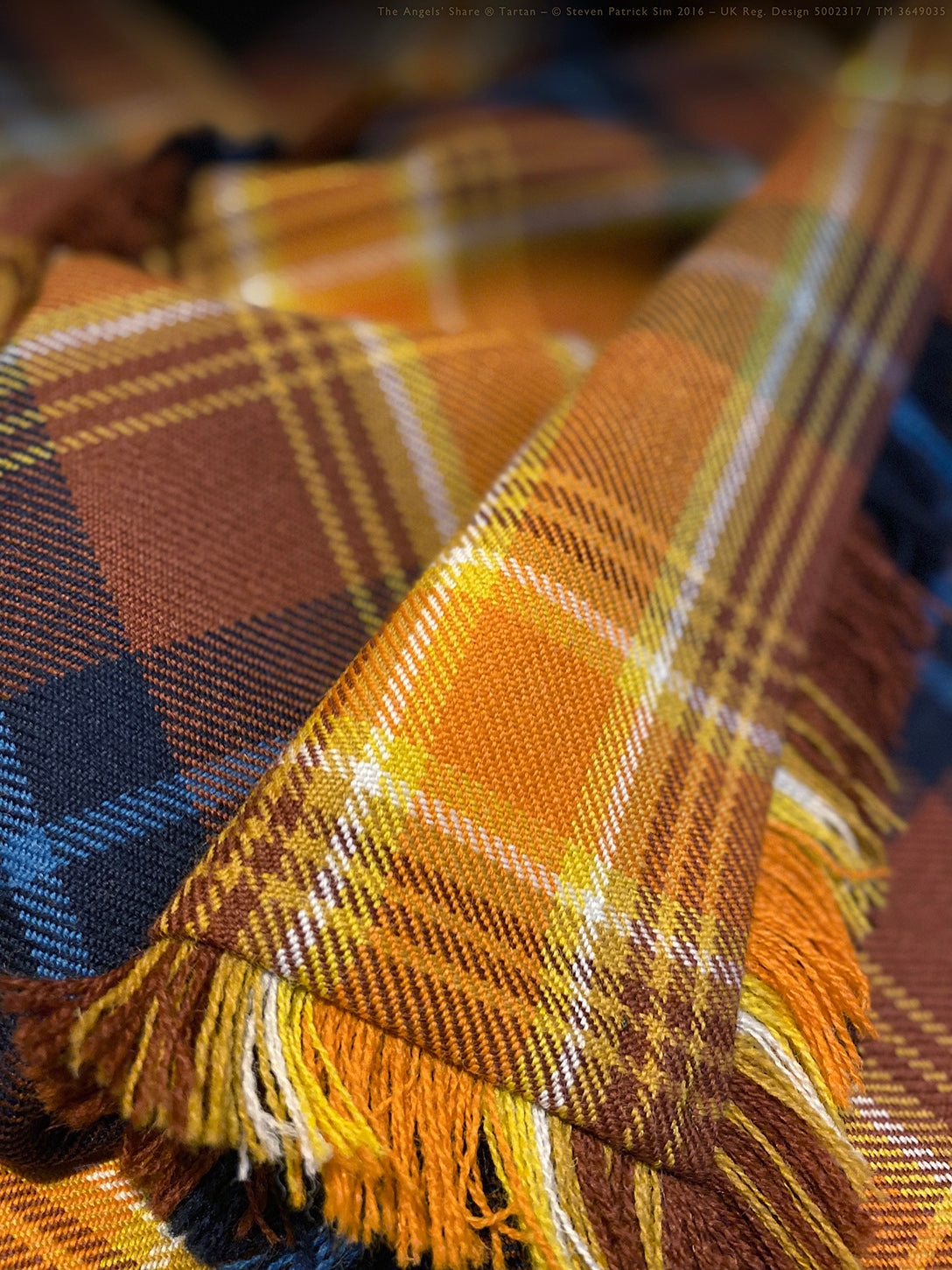 Close-up view of the deep weave detail of the Angels’ Share fly plaid with vibrant tartan colours. A detailed macro of the Angels’ Share® fly plaid showcasing its rich texture and saturated whisky-inspired hues — highlighting the woolen weave and fringe in sharp focus.