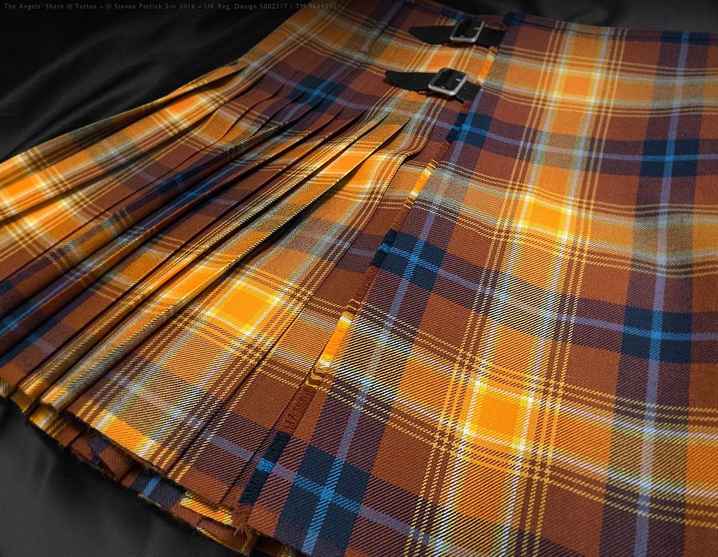 Wide-angle of Angels’ Share® kilt pleated to sett, radiating golds and browns in luminous folds of heavyweight 16oz tartan. Pleated to the sett — the balanced symmetry of Scotch colour.