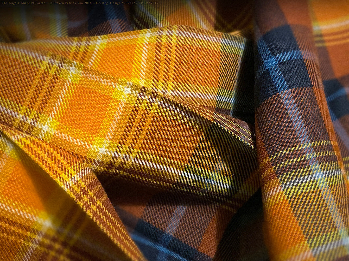 Close-up of the Angels’ Share tartan, pleated and softly lit, revealing ethereal interplay of ochre, amber and indigo. A shimmering sett alive with the alchemy of whisky light.