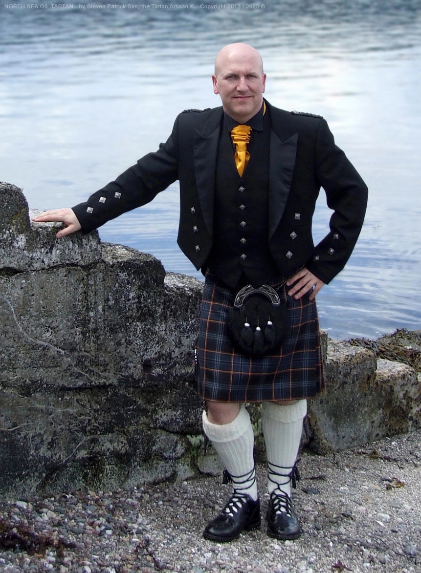 Portrait of Steven Patrick Sim wearing the North Sea Oil tartan kilt on the Isle of Bute, set against a coastal landscape that echoes the tartan’s maritime origins.