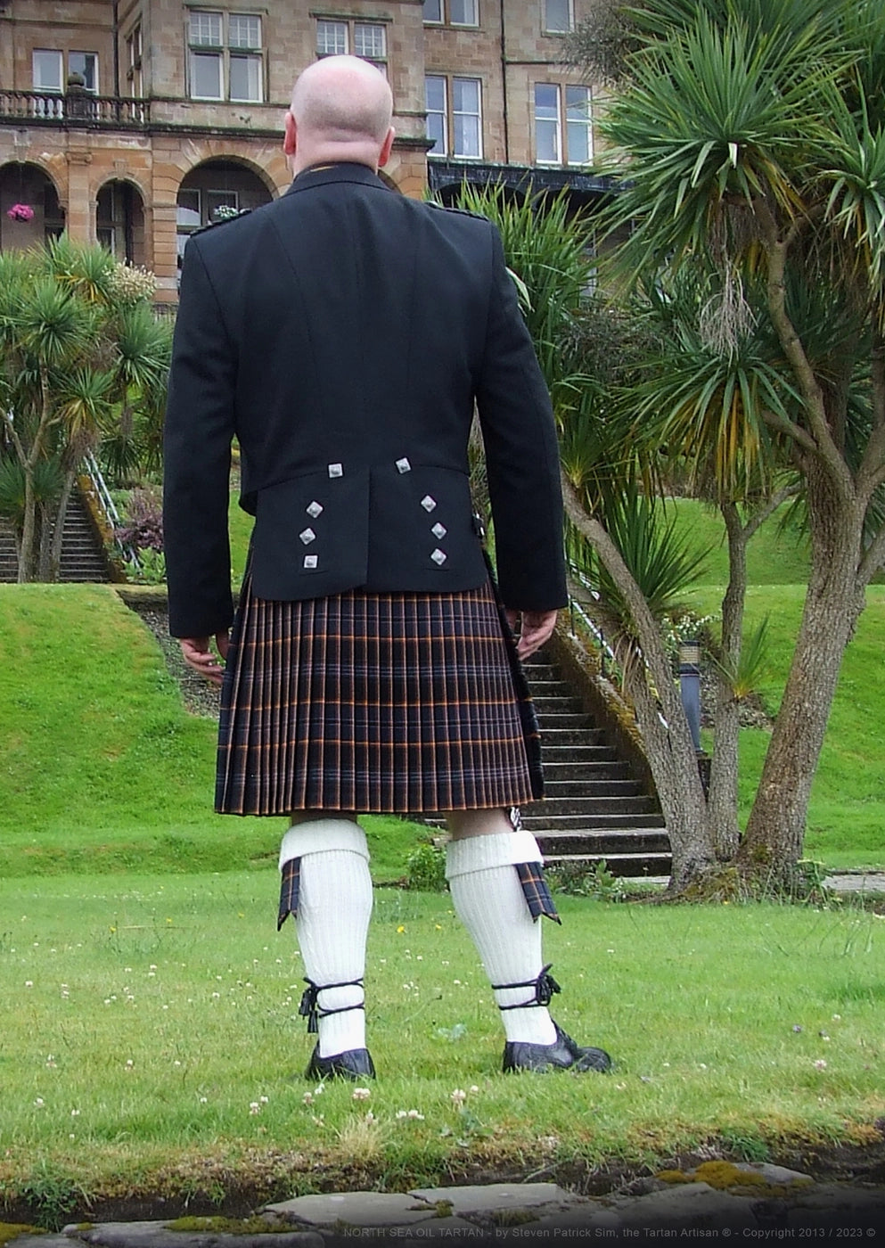 Outdoor portrait of Steven Patrick Sim wearing the North Sea Oil tartan kilt in the Glenburn Hotel gardens, blending heritage dress with formal landscape.