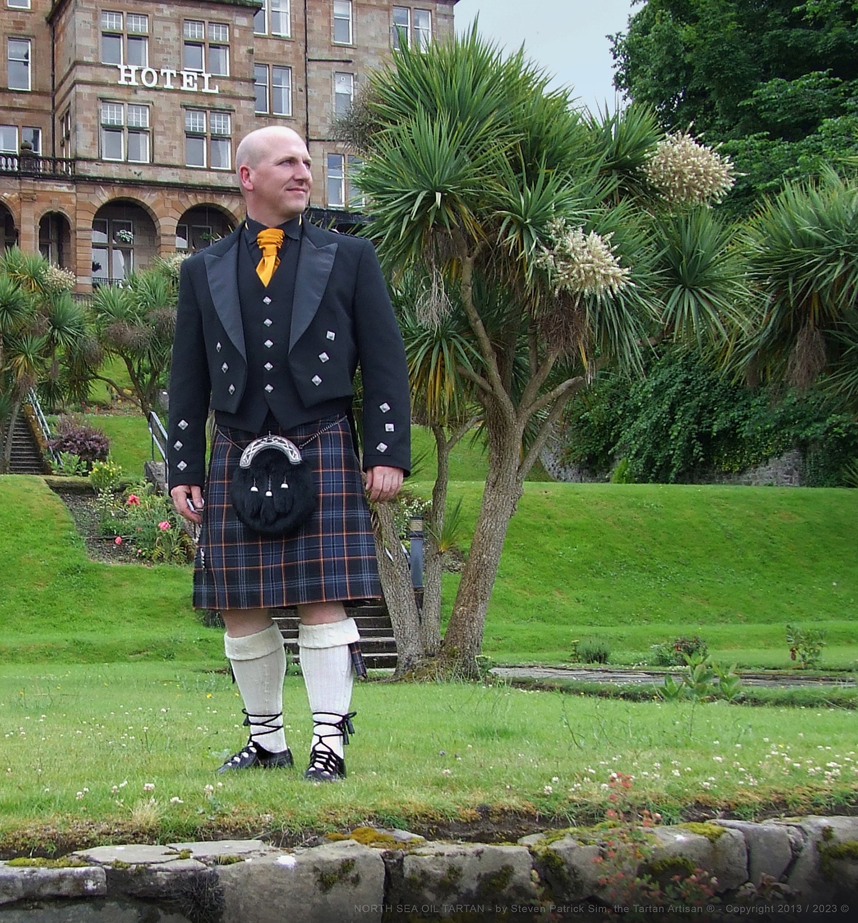 Steven Patrick Sim, the Tartan Artisan, wearing the North Sea Oil tartan kilt at the historic Glenburn Hotel on the Isle of Bute. The image highlights the distinctive flame-striped tartan, symbolizing Scotland’s offshore oil heritage, set against the elegant backdrop of the hotel's classic architecture.