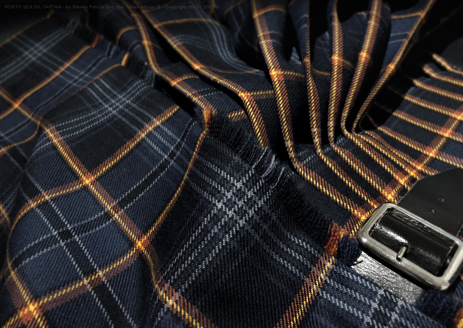 Close-up detail of North Sea Oil tartan kilt featuring a single buckle closure, traditional triple-layered fringe on the front apron, and pleats precisely aligned to the flame stripe, expertly crafted by Steven Patrick Sim the Tartan Artisan to highlight intricate tailoring and symbolic design elements.