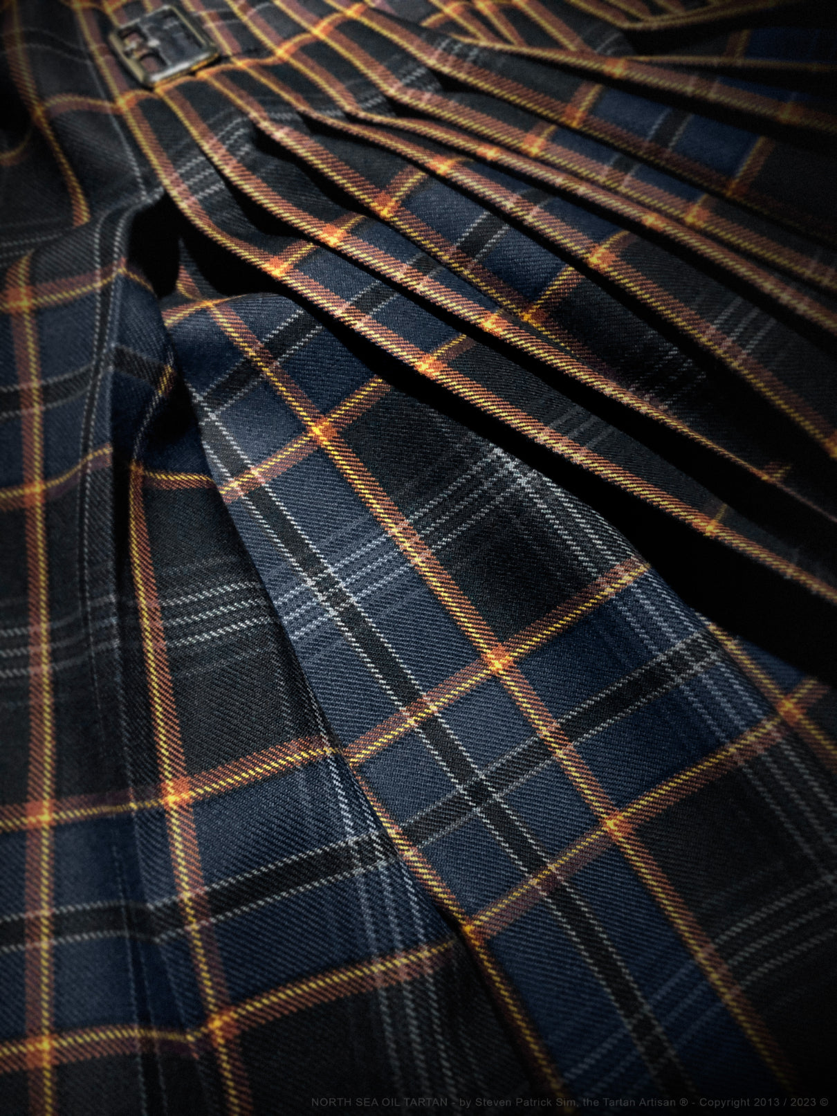 Heavyweight 16oz North Sea Oil tartan kilt, traditionally tailored in Scotland by Steven Patrick Sim the Tartan Artisan, featuring deep, bold colors representing crude oil and the North Sea, with pleats set to the symbolic ‘Flame of Remembrance’ motif, adjustable leather straps, a single fringe edge, and a classic made-to-measure fit, commemorating Scotland’s offshore oil heritage.