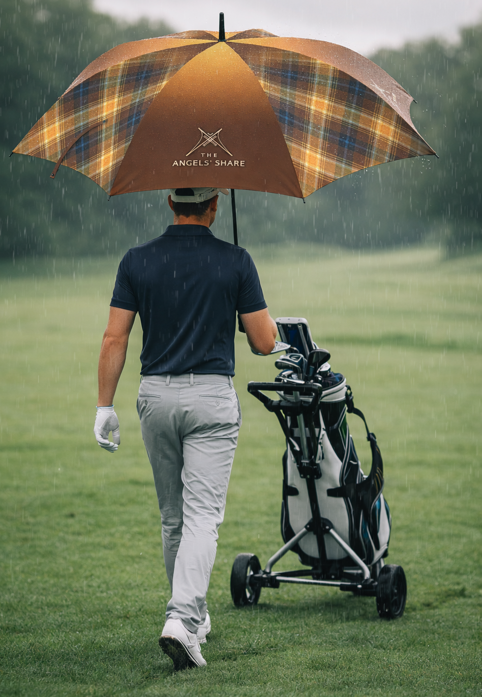 Golfer walking in heavy rain pushing a trolley under The Angels’ Share tartan umbrella.