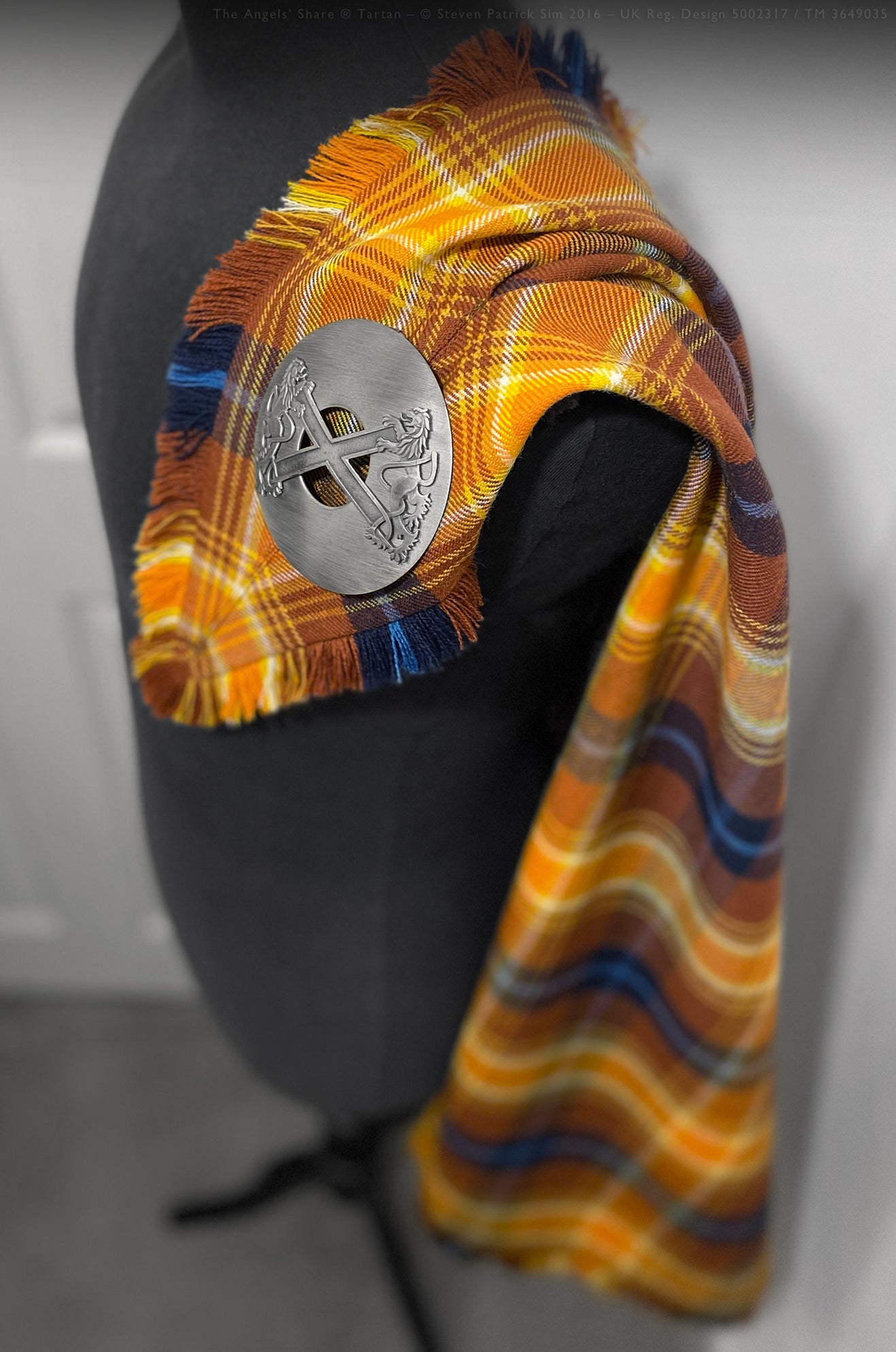 Angels’ Share tartan fringed fly plaid shown draped, displaying rich whisky-inspired colours and traditional woven texture.