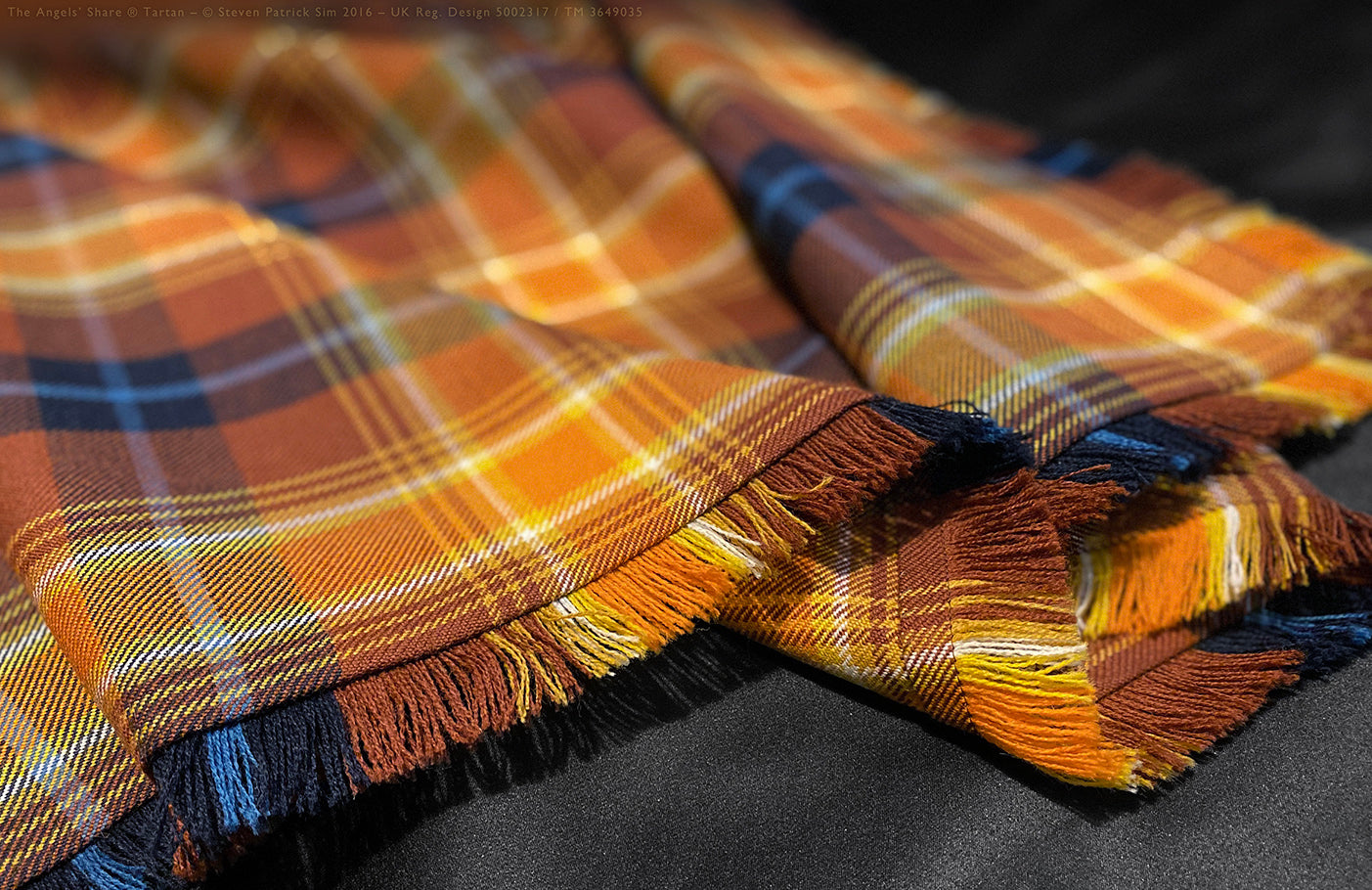 A sharp focus on the colourful fringe edge of the Angels’ Share fly plaid. Featuring a richly coloured fringe edge with golden, ochre, russet, and indigo yarns — this close-up reveals the tactile craftsmanship of the Angels’ Share® fly plaid.