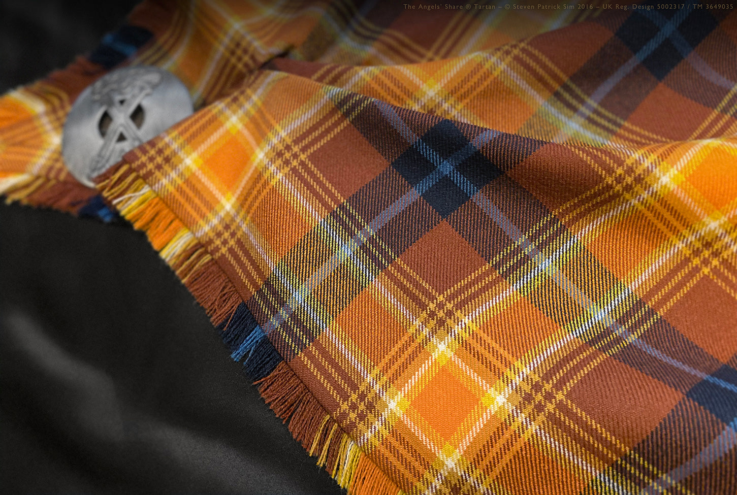 Detail of brooch pinning the Angels’ Share tartan fly plaid. The iconic Angels’ Share® tartan is pinned with a silver Celtic brooch — rich hues and clean pleats frame the composition, blending formality with storytelling.