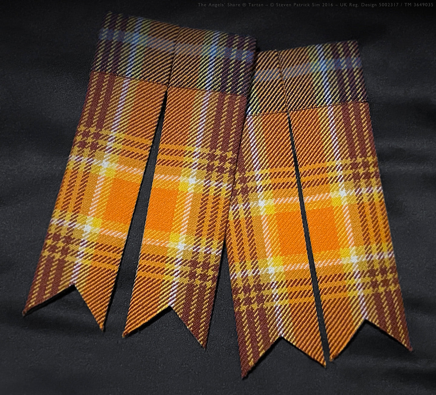A pair of Angels’ Share® tartan flashes laid flat, showing their bright whisky-inspired colour palette. A crisp close-up of the Angels’ Share® tartan flashes — hand-cut to display the vivid sett design. These flashes are a striking kilt accessory, complementing the vibrant tones of the whisky tartan.