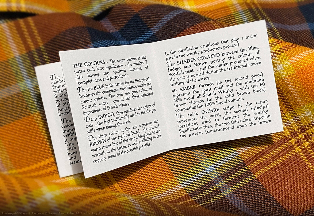 Open Angels’ Share tartan booklet page explaining the seven colours of the tartan and their symbolic meanings, photographed on the tartan cloth.