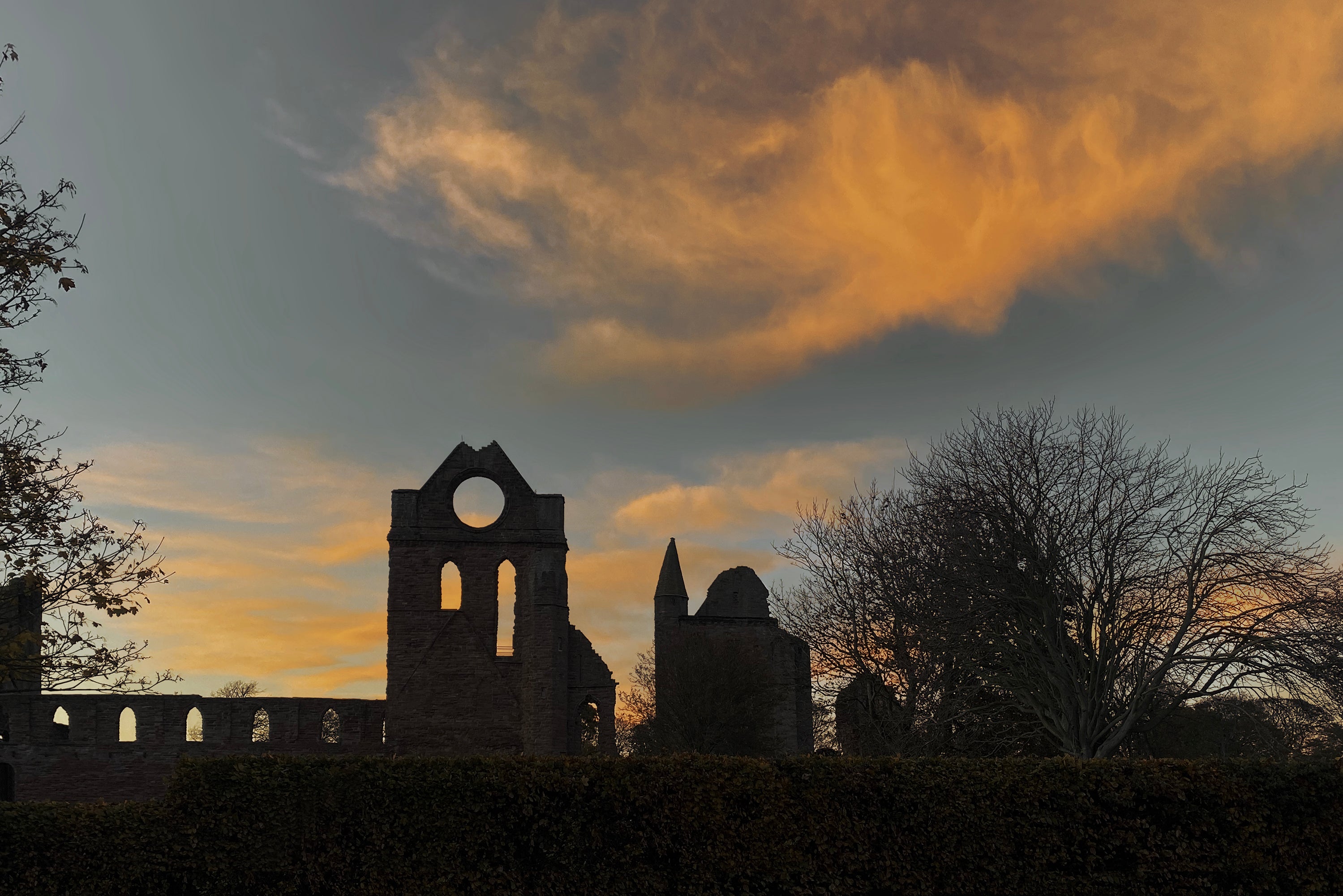 Wide panorama of Arbroath Abbey and the Round O at sunset with orange clouds and historic stone silhouette.