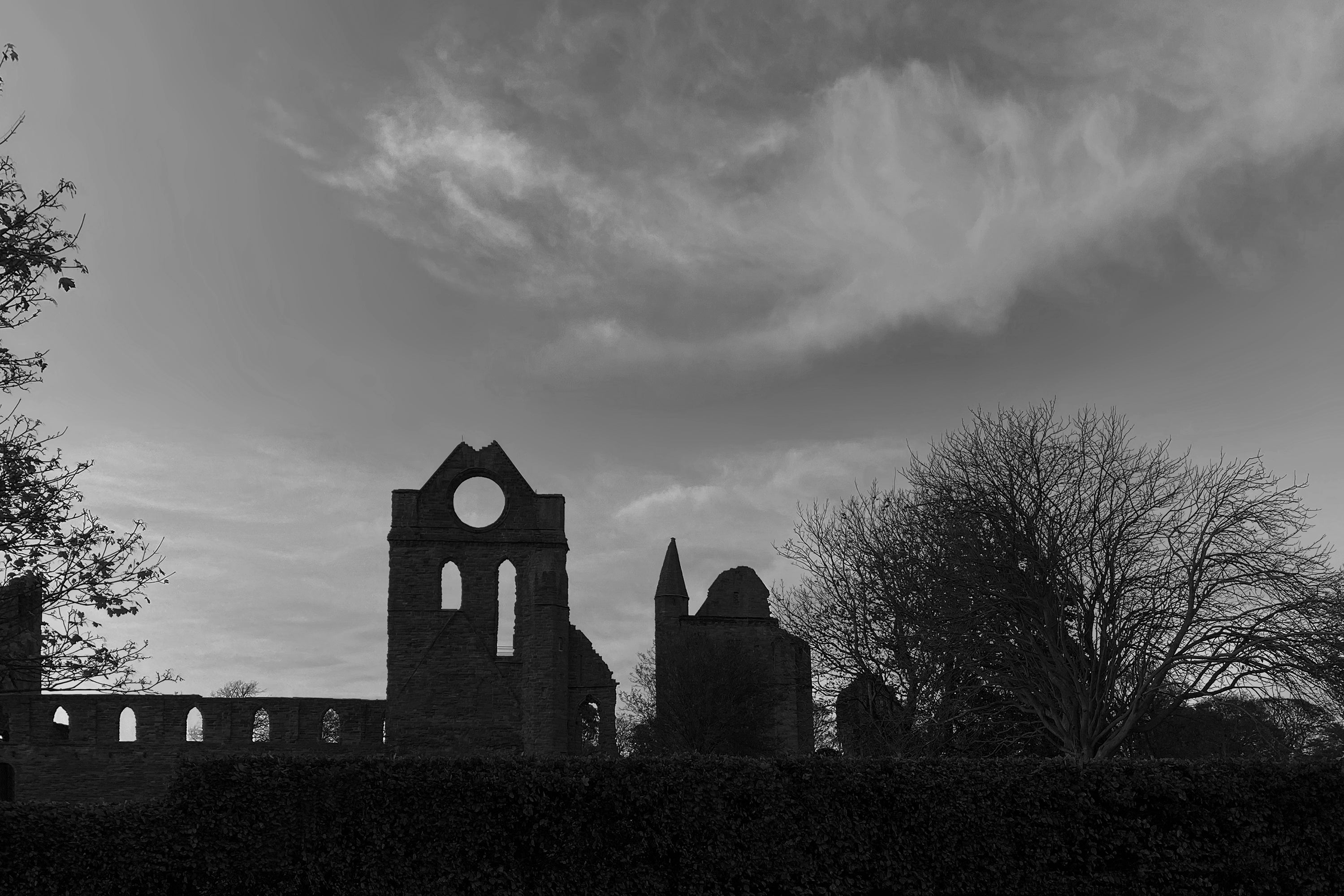 Wide panorama of Arbroath Abbey and the Round O at sunset with monochrome clouds and historic stone silhouette.