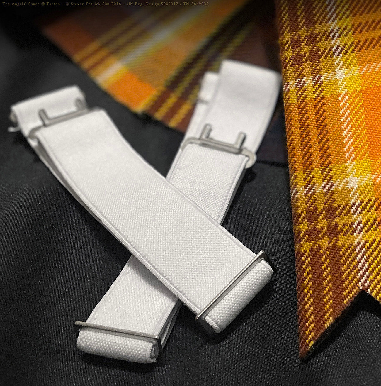 Two neatly cut tartan flashes in the Angels’ Share® design, placed on dark cloth for contrast. A sharply detailed image of the Angels’ Share® tartan flashes, highlighting the rich hues of amber, ochre, and oak — inspired by the spirit of Scotch whisky.