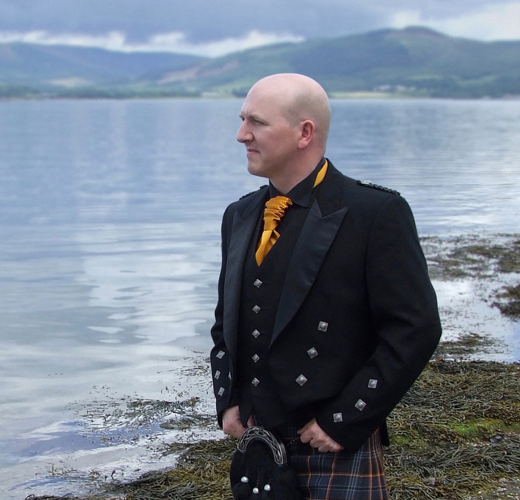 Steven Patrick Sim, the Tartan Artisan, wearing the North Sea Oil tartan kilt on the Isle of Bute. The photo highlights the distinctive flame-striped tartan design, symbolizing Scotland’s offshore oil heritage, with the scenic Isle of Bute landscape providing an elegant and historic backdrop.